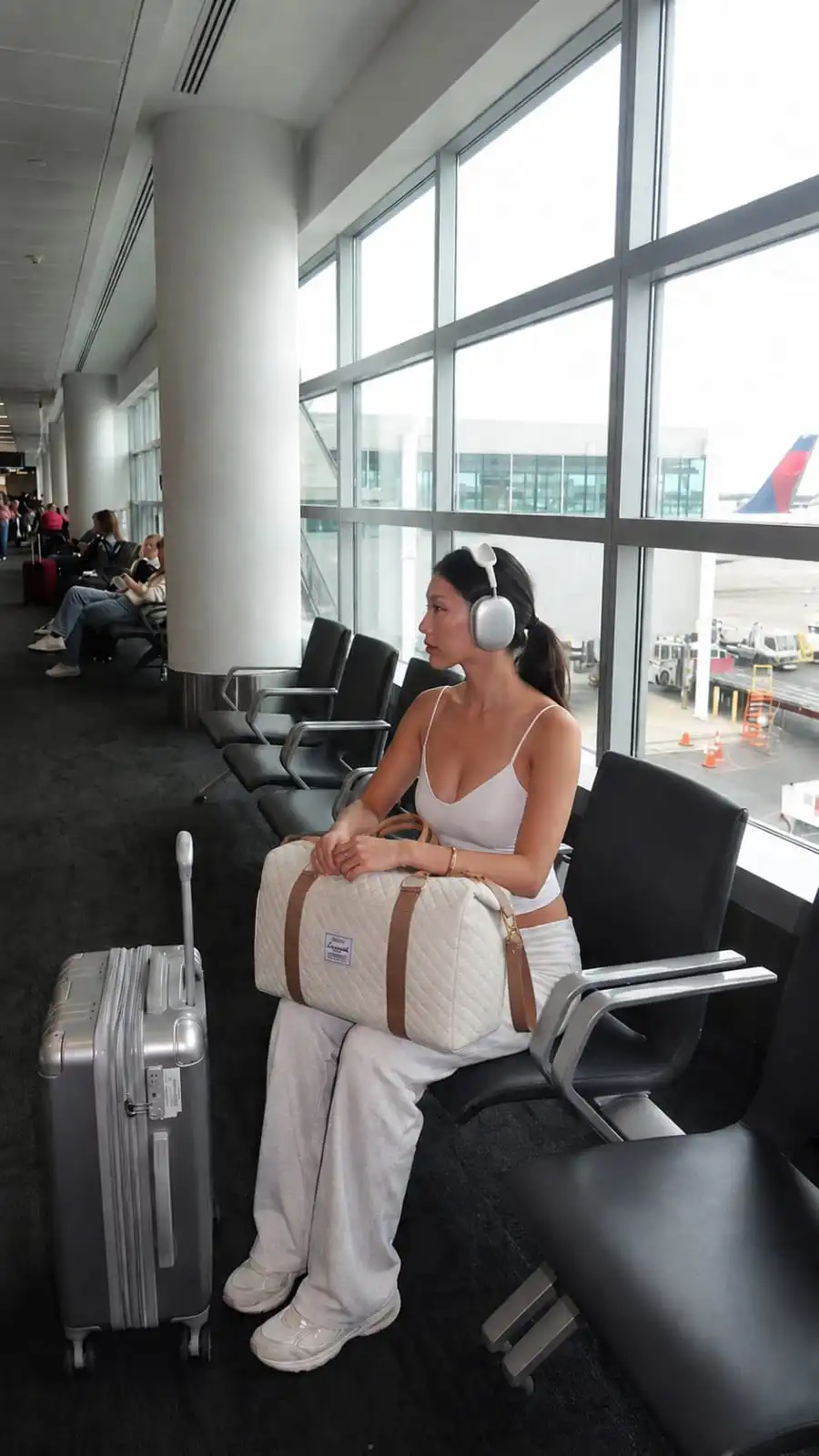 Woman sitting at an airport gate holding a quilted travel duffel bag, showcasing one of the best travel duffel bags for women with extra space, carry-on convenience, and organized storage for weekend trips and flights.
