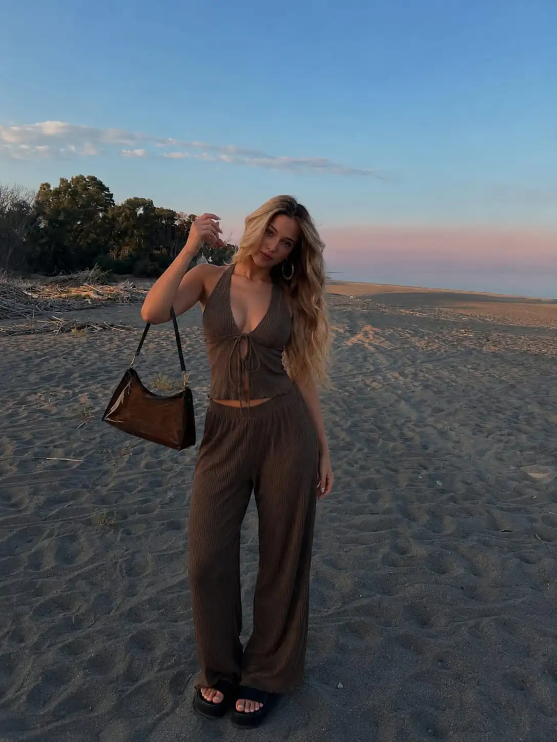 Woman wearing a brown halter top and wide-leg pants set with a transparent shoulder bag, creating a chic beach vacation outfit for women.