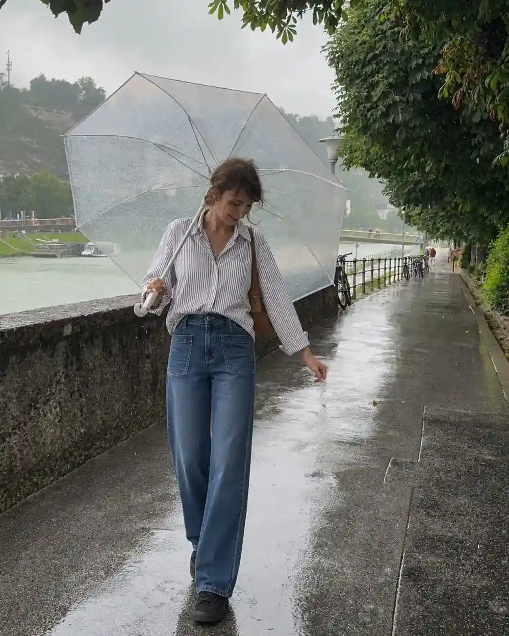 Woman wearing a striped button down shirt, wide leg jeans, and slip resistant sneakers for a rainy day spring outfit.