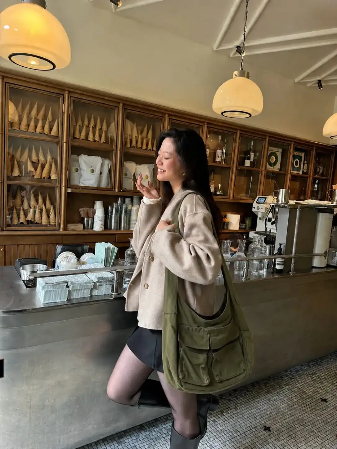 Woman carrying a casual canvas messenger bag in a coffee shop, showcasing an affordable designer-inspired shoulder bag for everyday use