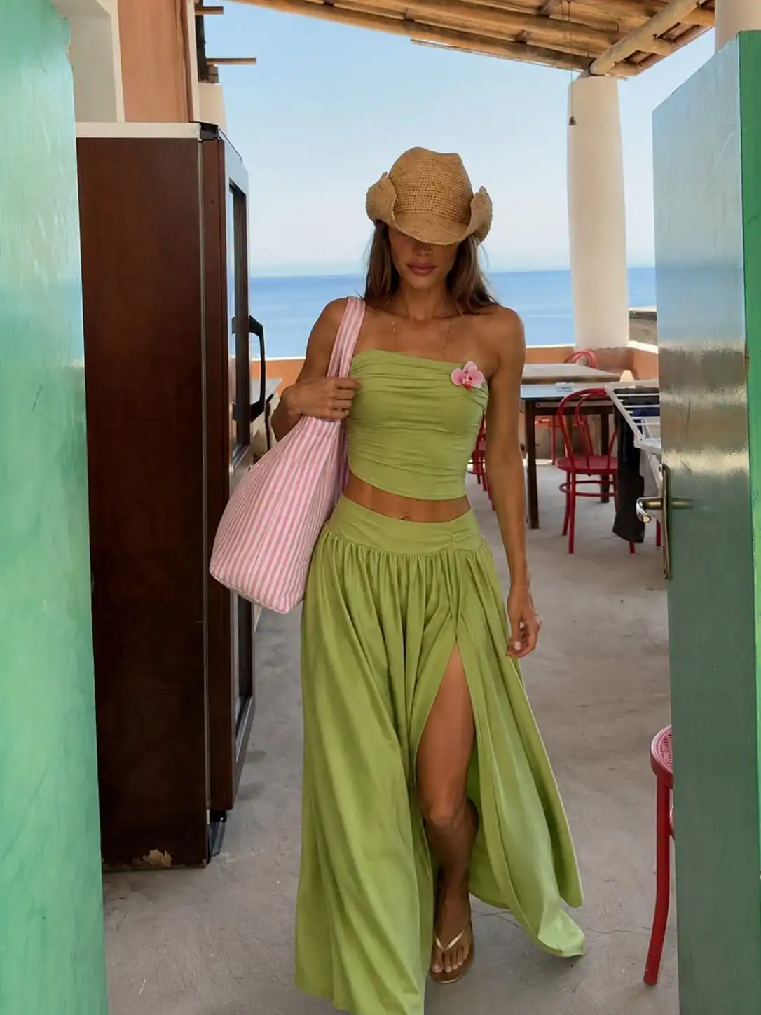 Woman wearing a green bandeau top and high-slit maxi skirt with a striped canvas tote, creating a stylish beach vacation outfit for women.