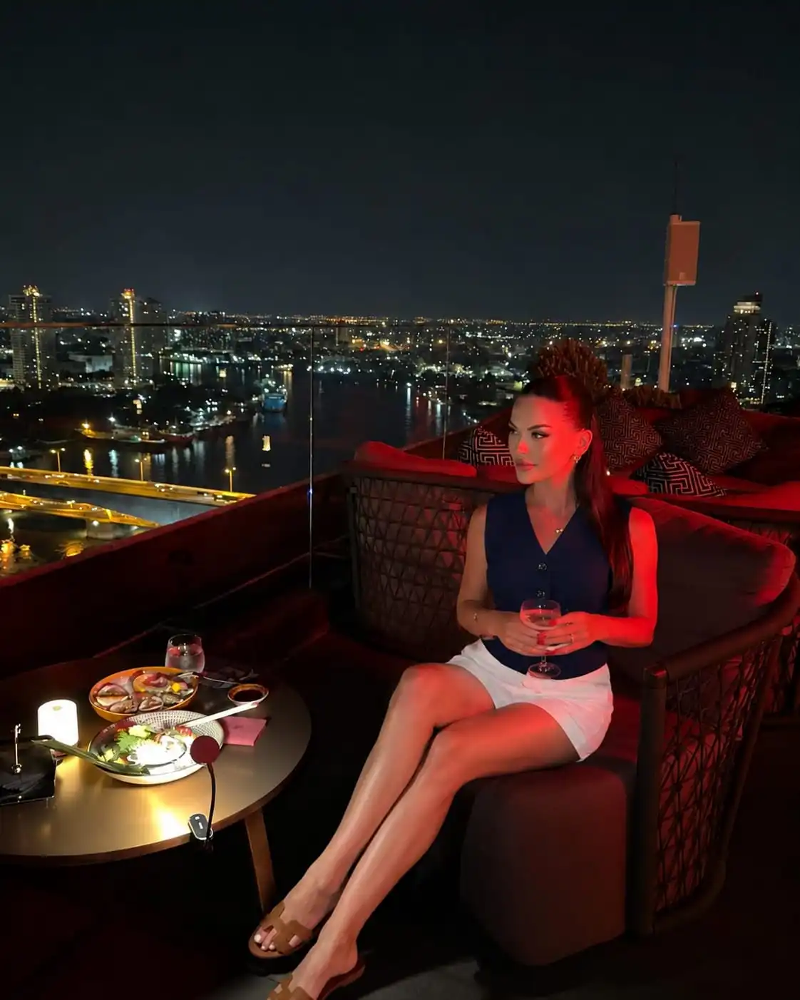 Woman wearing a navy vest and white pleated shorts for chic rooftop bar outfit ideas in summer