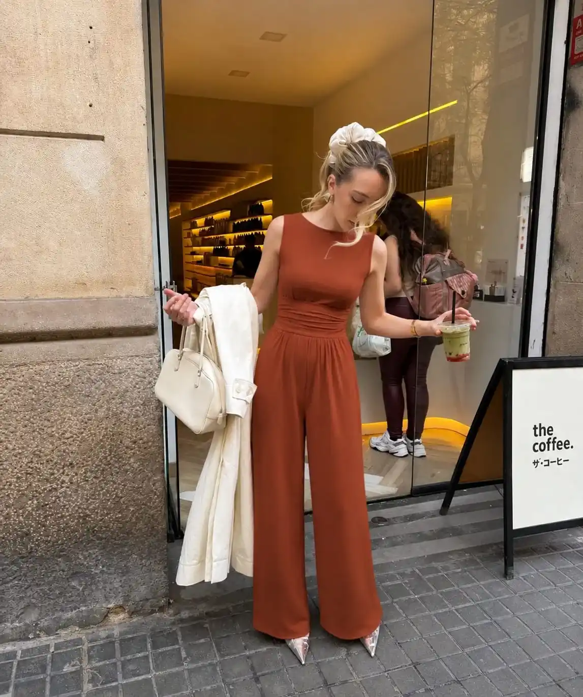 Rust-colored sleeveless jumpsuit accessorized with gold jewelry, creating a sophisticated graduation guest outfit