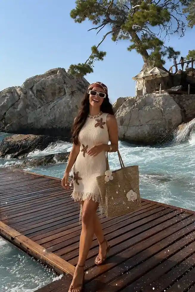 Woman wearing a white starfish knit mini dress with a floral woven beach tote, perfect for a tropical beach vacation outfit.