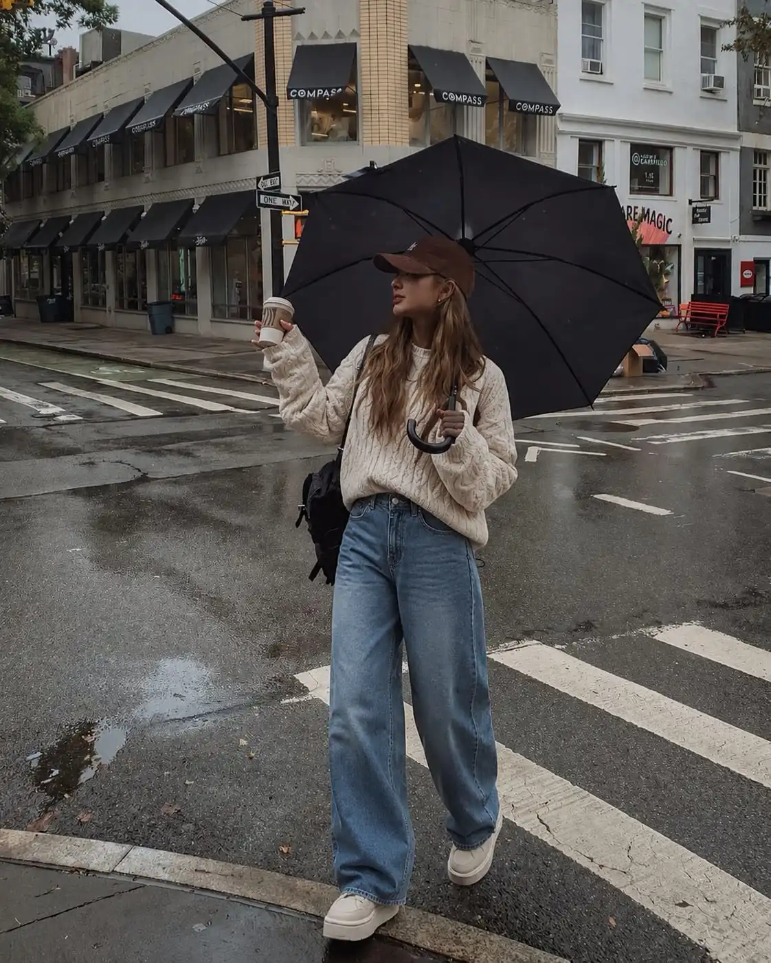 Woman styling an oversized cable knit sweater with wide leg jeans and platform sneakers on a rainy spring day.