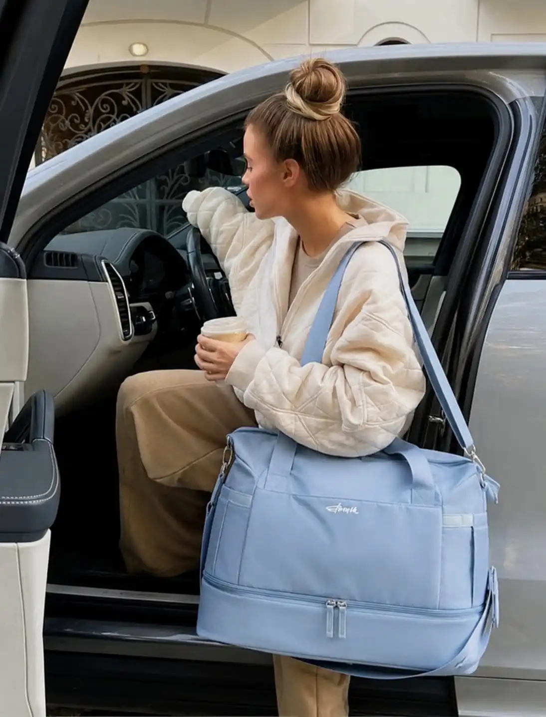 Woman carrying a light blue travel duffel bag with shoe compartment while getting into a car, showcasing one of the best travel duffel bags for women for weekend trips, road travel, and carry-on packing.