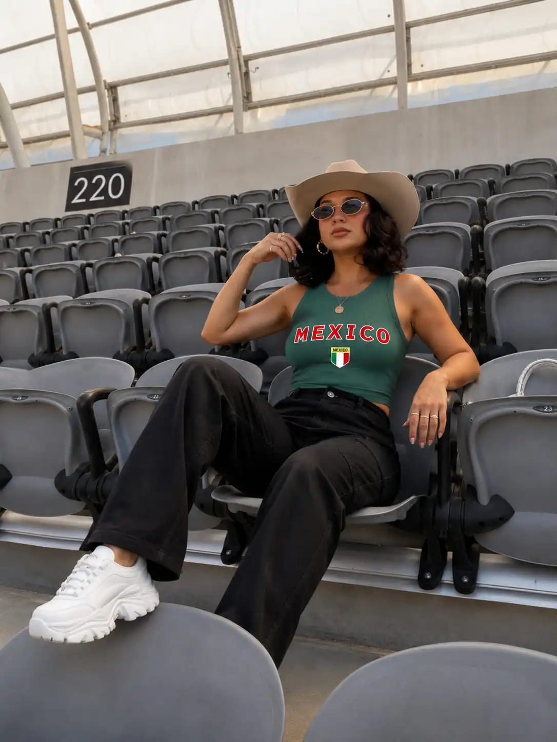Woman wearing a mexico soccer game outfit with a green crop tank, black utility pants, and chunky white sneakers.