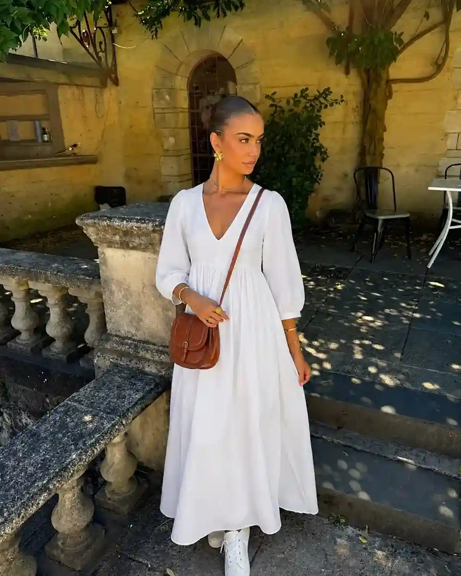 Woman wearing a white boho maxi dress with white sneakers and a brown saddle crossbody bag, creating a chic and comfortable everyday summer outfit.
