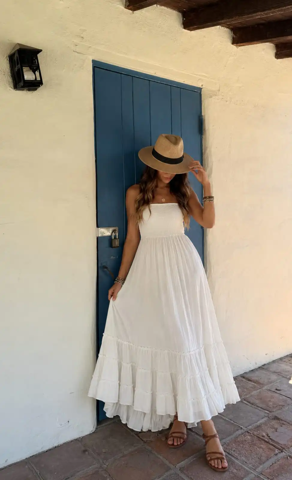 Woman wearing a white boho maxi dress with a smocked bodice, straw Panama hat, and flat sandals, creating an elegant vacation-inspired summer outfit.