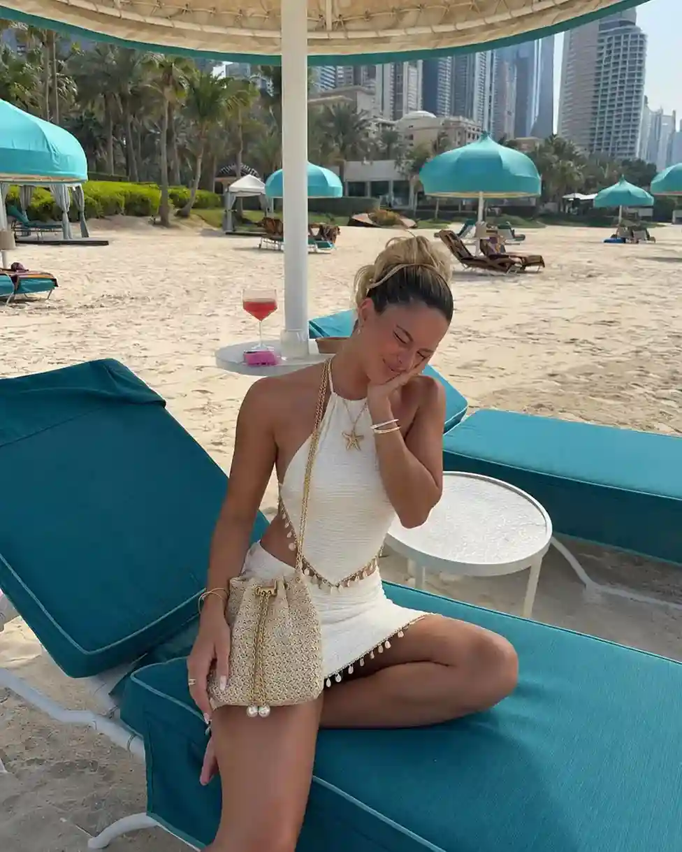 Woman wearing a white halter mini dress with a woven straw bucket bag, styled for a summer beach vacation outfit.