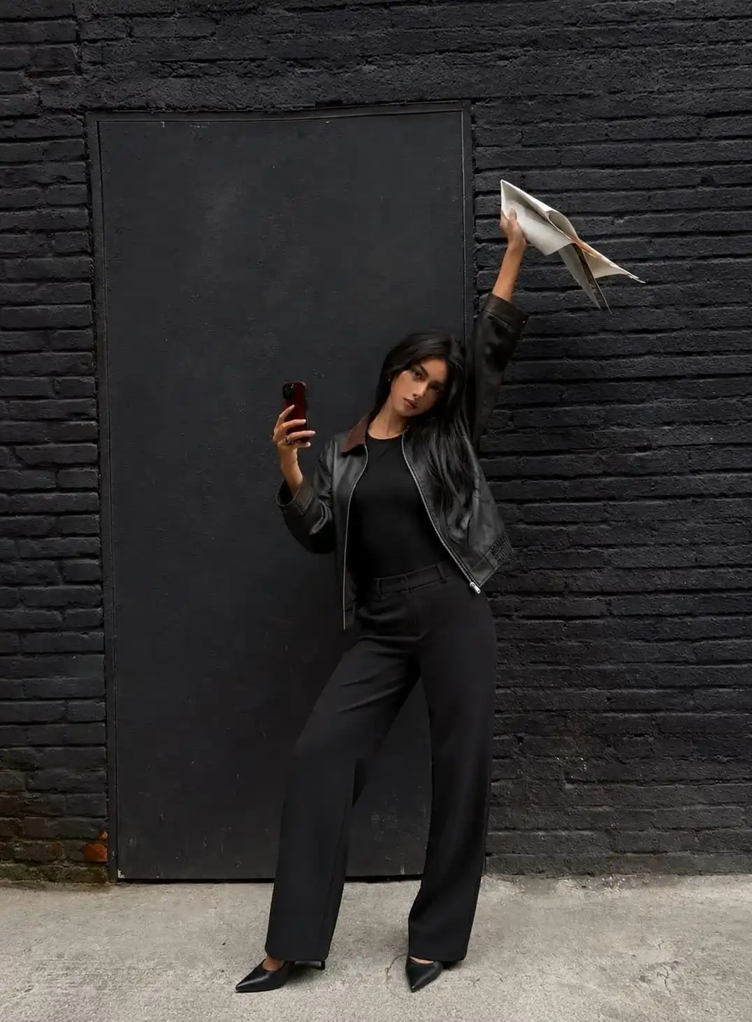 Woman wearing a black leather jacket with a black fitted top and black wide-leg trousers for a chic monochrome leather jacket outfit suitable for work or evening wear in 2026.