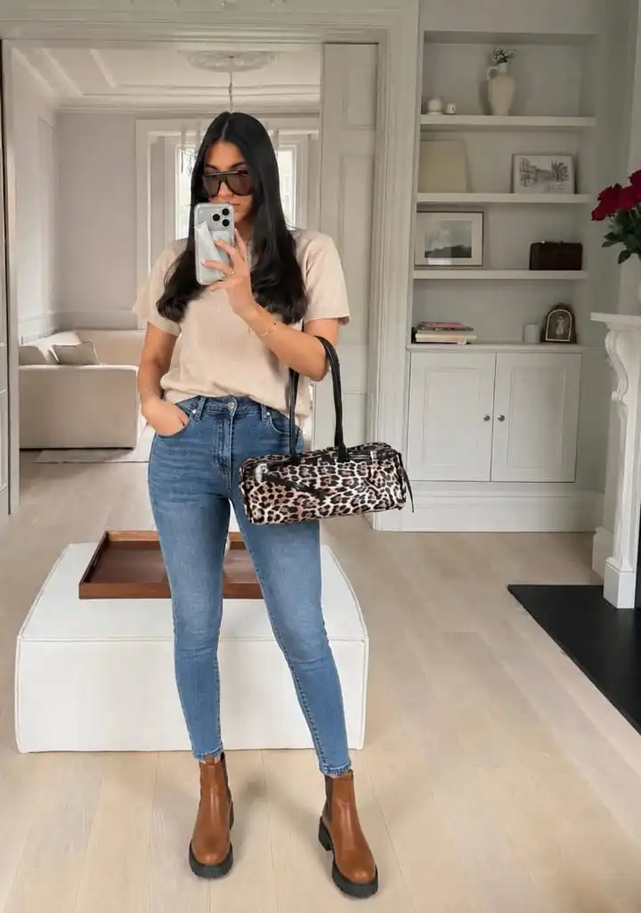 Woman styling a beige knit top with blue skinny jeans and brown ankle boots in a casual western outfit.