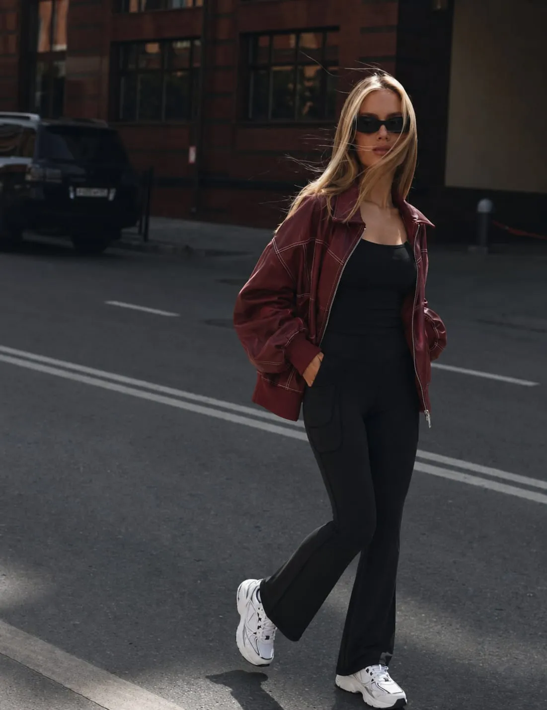 Woman wearing an oversized burgundy leather jacket with a black fitted top, black flare pants, and white sneakers for a casual leather jacket outfit in 2026. 