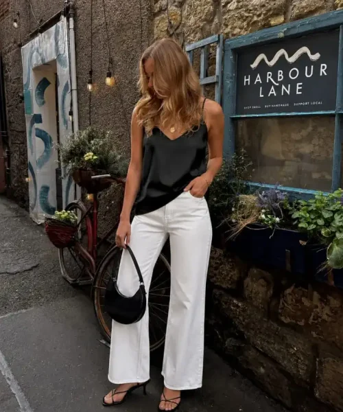 Woman wearing a black satin camisole with white wide-leg jeans and black strappy heels in an elegant western outfit.